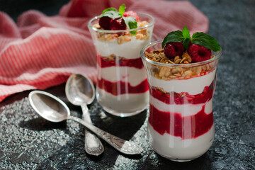 Two glasses with raspberries, granola and cream cheese on a black background. Healthy homemade organic dessert.