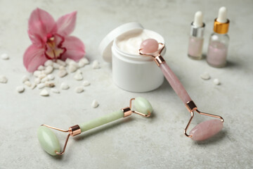 Natural jade face rollers, cosmetic products and flower on grey background