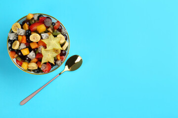 Delicious exotic fruit salad and spoon on light blue background, flat lay. Space for text