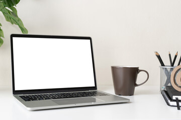 Laptop computer with blank screen for mockup on modern contemporary workspace desk with coffee cup and office supplies. Home office workplace.