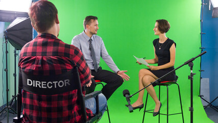 Female presenter interviewing in television studio with director in foreground