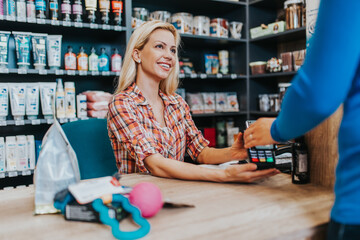 Fototapeta premium Smiling saleswoman working at pet shop checkout. Electronic payment with card.