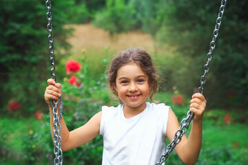 Child playing on outdoor playground. Kids play on school or kindergarten yard. Active kid on colorful swing. Healthy summer activity for children in sunny weather. Little girl swinging.
