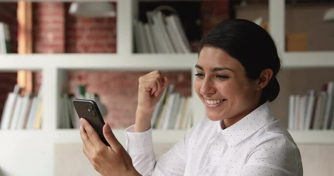 Indian businesswoman reading message on cellphone feels euphoric laughs enjoy business success, sales growth, got opportunity. Victory moment and happy winner of online auction celebrate win concept
