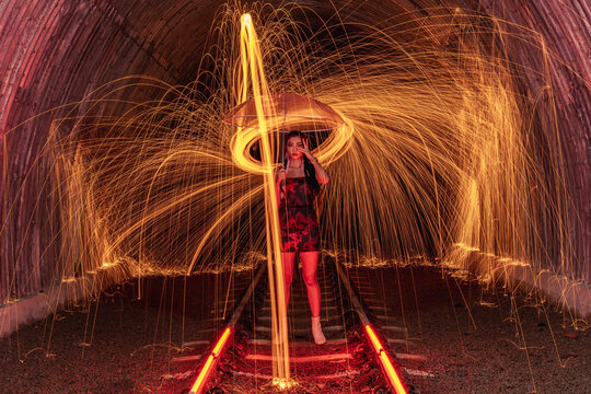 Beautiful woman holding an umbrella standing on railway tracks surrounded by spinning wire wool