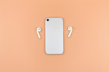 A phone with two wireless headphones on the sides on a bright background. A modern concept. Minimalism