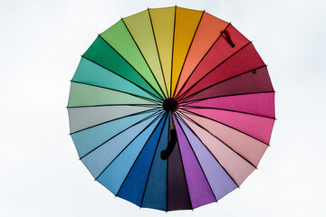Large rainbow opened umbrella viewed from below towards white background .