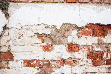 Old wall surface with crumbling plaster. Old brick wall for background. Red bricks and cement pavement. The dilapidated facade of the house with damaged plaster.