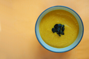 cream soup of pumpkin and carrot with pumpkin seeds stands in a round gray plate on an orange background top view . homemade food