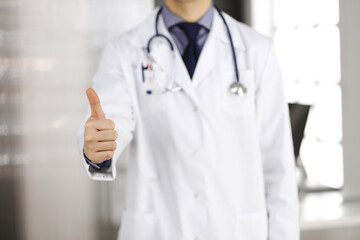 Unknown male doctor standing with thumbs up sign in clinic near his working place, closeup. Perfect medical service in hospital. Medicine and healthcare concept