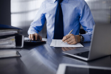 Unknown man accountant in blue shirt use calculator and computer with holding pen on while staying...