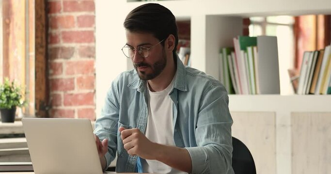 Brooding millennial young man sit at desk thinking over business plan, develop start up, search and consider new fresh ideas texting on portable computer. E-learning process using modern tech concept