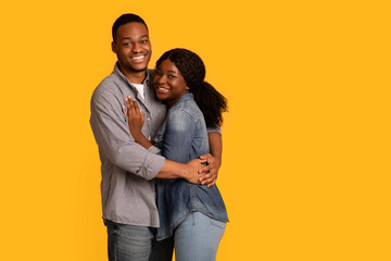 Portrait of loving black couple embracing while posing over yellow background