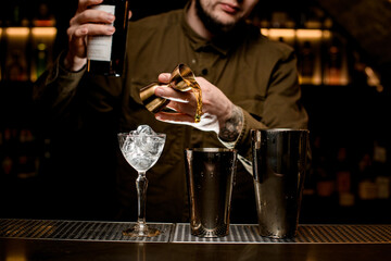 view on shaker cups and glass on bar counter and bartender pouring drink