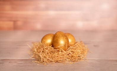 three golden easter eggs in a nest on a wooden table