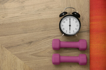 Alarm clock, yoga mat and dumbbells on wooden background, flat lay with space for text. Morning...