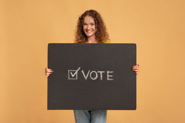Smiling young redhead curly female holding holding vote sign, poster or banner with inscription