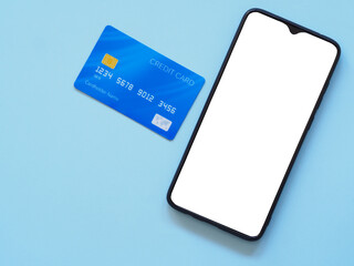 Fototapeta premium Top view smartphone shows a white screen display and credit card on blue background. Copy space, flat lay.