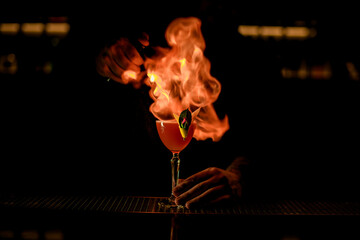 amazing view of glass with cocktail that bartender sets to fire at dark bar