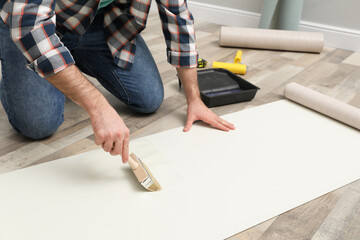 Man applying glue onto wall paper on floor, closeup