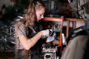 young woman repairing part of motorcycle engine in garage