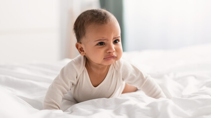 Portrait of sad black baby crying and crawling on bed