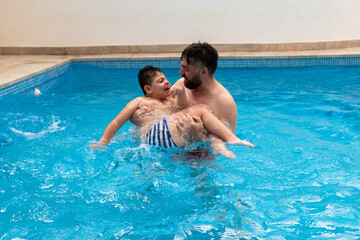 child with disability laughs and plays in his father's arms in a swimming pool