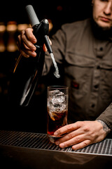 barman adds carbonated liquid from siphon to transparent glass with cocktail