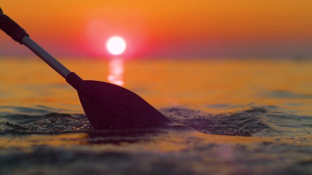 SLOW MOTION, CLOSE UP, LENS FLARE, SILHOUETTE, DOF: Gorgeous golden sunset shines on the kayaker's paddle splashing ocean water. Scenic shot of the endless Adriatic sea at sunrise and rower's paddle.