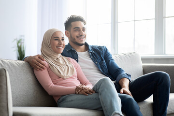 Obraz premium Cheerful muslim family sitting on sofa at home