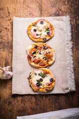 Three mini pizzas with salami, bacon, mozzarella and olives on a plain linen napkin - an italian homemade snack