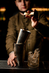 Fototapeta na wymiar view of steel shaker cups with condensation and hand of bartender with jigger