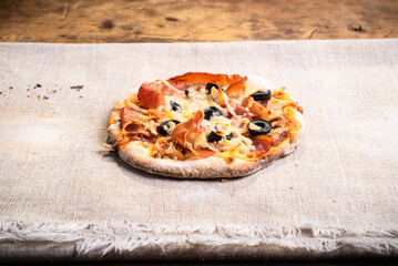 Mini pizza with jamon, mozzarella and olives on a plain linen napkin - an italian homemade snack