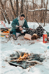 A beautiful couple in love on a winter picnic, playing with a dog and enjoying themselves 