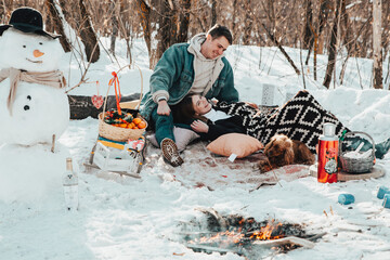 A beautiful couple in love on a winter picnic, playing with a dog and enjoying themselves near the campfire