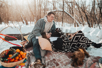 Beautiful couple in love on a winter picnic, playing with the dog and laughing near the campfire