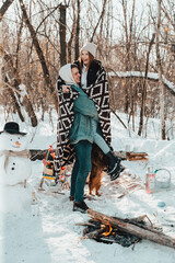 Beautiful couple in love on a winter picnic, hugging and laughing near the campfire
