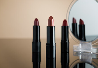 Set of lipsticks on cream reflective surface, two of them reflecting on a cosmetic mirror.