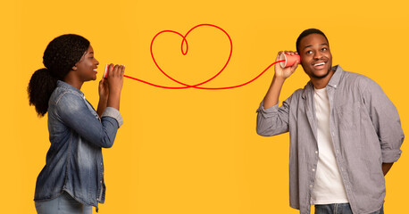 Love Message. Black woman whispering romantic words to boyfriend via tin phone