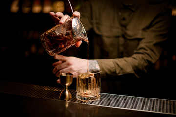 bartender s hand holds mixing cup with cold cocktail and pours it into old-fashioned glass