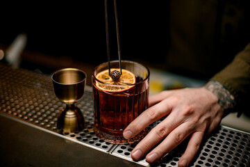 man decorating by small pine cone an old-fashioned glass of cocktail with orange slice