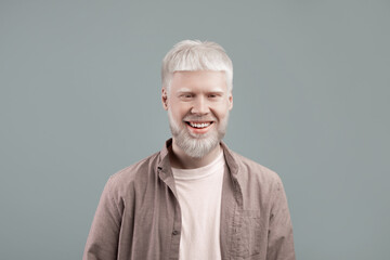Happy albino man with white skin and hair posing with confident smile on grey studio background