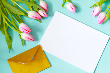 blank white paper page with golden envelope and beautiful pink tulip flowers on blue background