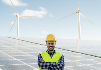 Young male engineer working for alternative energy with wind turbine and photovoltaic panels -...