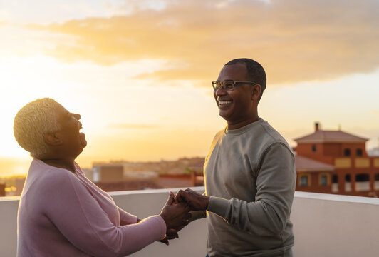 Happy Latin senior couple having romantic moment dancing on rooftop during sunset time
