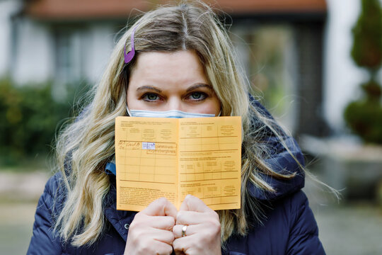Woman with medical mask holding German inernational certificate of the vaccination. Adult showing the information about her vaccine against covid 19 corona virus.
