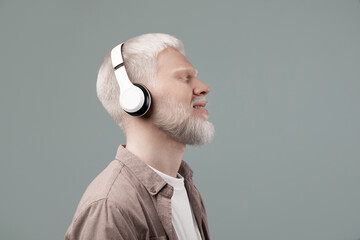 Enjoy the sound. Peaceful albino guy listening to music with closed eyes in wireless headset,...