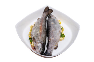 Fresh, raw two trout lying on a plate, stuffed with butter, parsley and lemon slices, isolated on a white background with a clipping path, top view.