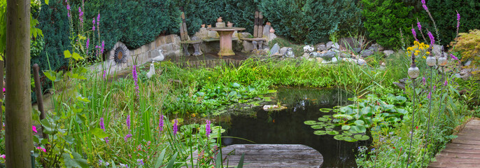 Gartenteich mit Pflanzen und Sitzgruppe im Sommer, Panorama