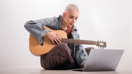 Young hipster woman watching guitar tutorials on laptop. Distance learning music